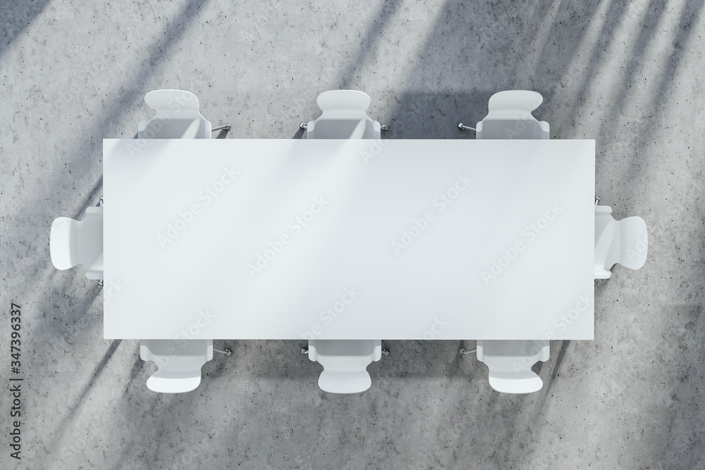 White conference table surrounded by chairs viewed from above on a concrete floor