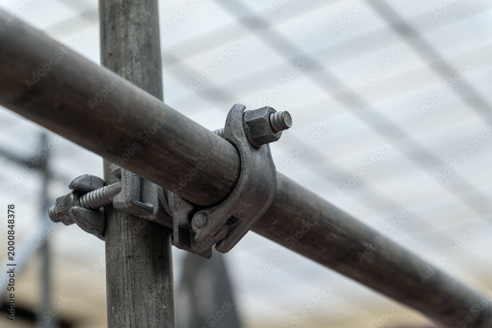Close-up of a galvanized scaffolding clamp joining metal pipes